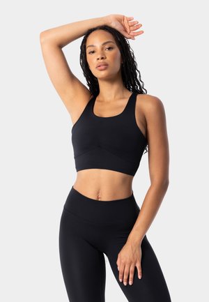 Černý sportovní crop top se širokými ramínky a hladkým povrchem, kombinovaný s černými legínami s vysokým pasem. Jednoduchý design bez viditelných log.