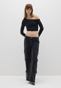 Top corto nero a maniche lunghe con arricciatura sul davanti. Abbinato a pantaloni cargo neri a vita alta con dettagli sulle tasche e spacchi laterali.