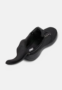 Chaussure de sport noire avec une ouverture zippée, tige en tissu texturé, col rembourré et semelle en caoutchouc moulé. Logo visible à l'intérieur.