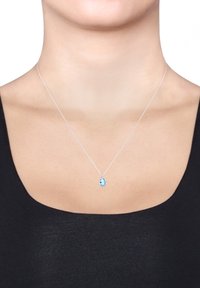 Silberne Halskette mit einem ovalen blauen Edelstein-Anhänger. Die Kette ist dünn und zart und liegt direkt über dem Schlüsselbein auf einem dunklen Oberteil.