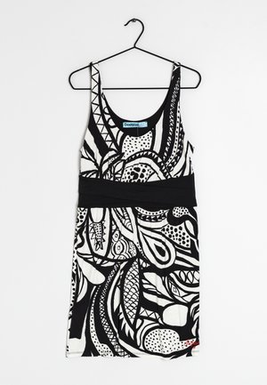 Robe sans manches noir et blanc avec des motifs abstraits, large ceinture noire, suspendue sur un cintre noir contre un fond blanc.