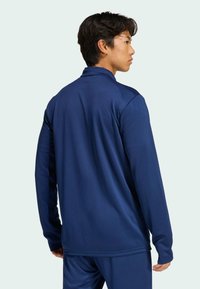 Ναυτικό αθλητικό μπλουζάκι μακρυμάνικο φτιαγμένο από λείο ύφασμα; διαθέτει όρθιο γιακά και κομψό σχέδιο στην πλάτη, σε συνδυασμό με ταιριαστά παντελόνια.