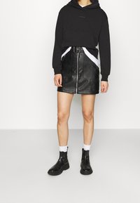 Sudadera negra con capucha, falda mini de cuero con cremallera frontal, combinada con botas negras de tobillo y calcetines blancos. Diseño simple y ajustado, sin patrones.