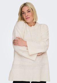 Pull crème en maille épaisse, avec un ourlet côtelé et des manches larges, comportant des rayures texturées horizontales et un col rond.