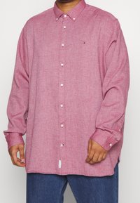 Langärmliges, rot kariertes Hemd aus weichem Stoff mit Kragen und Druckknopfverschluss, kombiniert mit blauen Jeans.