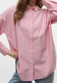 Camisa de manga larga, botón arriba, de color rosa claro con cuello clásico y corte relajado. Presenta botones frontales y una textura suave de algodón.