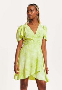 Green tie-dye dress with a deep V-neck, puff sleeves, and an asymmetrical hem. Made from lightweight fabric with a smooth texture.