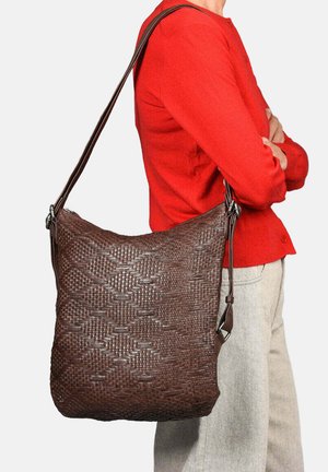 Bolso de hombro de cuero trenzado marrón con un patrón decorativo, correa ajustable y forma relajada. Combinado con una blusa roja y jeans claros.