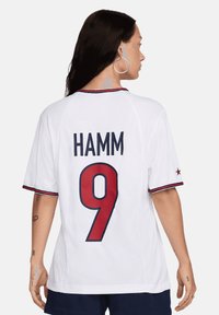 Maglia sportiva bianca con maniche corte, dettagli rossi e rifiniture blu. Presenta 'HAMM' in grandi lettere in grassetto e '9' in rosso sul retro.