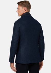 Blazer blu navy con finitura texturizzata, rever stretti e polsini con tre bottoni. Presenta un colletto a contrasto e un design su misura.
