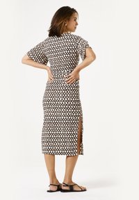 Getailleerde jurk met een diamanten patroon in zwart en crème, korte mouwen en een zijsplit. Gekoombineerd met zwarte sandalen.