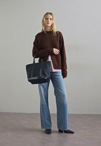 Pull marron oversize, chemise rayée en dessous, jean large bleu, sac à main en cuir noir avec poignées, et chaussures noires à bouts pointus.