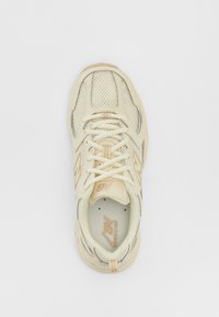 Baskets en mesh beige avec des accents et des lacets crème, présentant un bout arrondi et un col rembourré. Affiche le logo "New Balance" sur le côté.