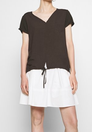 Bruin kort mouwtopje met V-hals, voorzien van een borstzakje en een trekkoordzoom. Draagt over een witte, uitlopende rok.