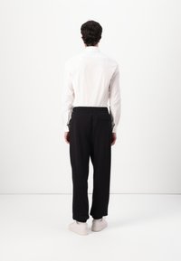 Witte blouse met lange mouwen, zwarte elastische polspijp broek en lichte sneakers. Glad stof, relaxte pasvorm en minimalistisch ontwerp.
