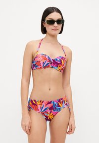 Bikini komplektas su raštuotu dizainu, kuriame dominuoja ryškios rožinės, violetinės ir mėlynos tropinės lapų spalvos. Viršus su sukimų detale; apatinės dalies šonai reguliuojami.
