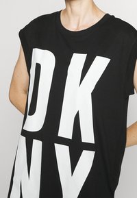 Svart bomullströja med vida ärmar och djärva vita bokstäver som stavar "DKNY". Strukturerad tyg och lös passform.