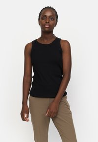 Top negru cu nervuri, fără mâneci, prezentând un decolteu rotund, o formă ajustată și o textură netedă, asortat cu pantaloni bej ajustați.