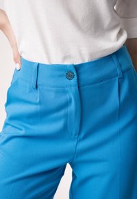Heldere blauwe op maat gemaakte broek van textuurstof, met een decoratieve knop op de tailleband en standaard voorkruis.