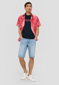 Korte mouwen rode shirt met wit bladerenpatroon, marineblauw t-shirt, lichtblauwe denim shorts en witte sneakers. Casual zomeroutfit.