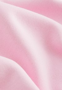 Svetle růžová bavlněná látka s hladkým povrchem, vykazující jemné záhyby a subtilní detaily prošívání. Ideální pro oděvy nebo textilní aplikace.