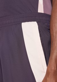 Dunkelviolette Sportshorts mit einem hellrosa Seiteneinsatz; verfügen über einen elastischen Bund und eine Reißverschlusstasche für Funktionalität.