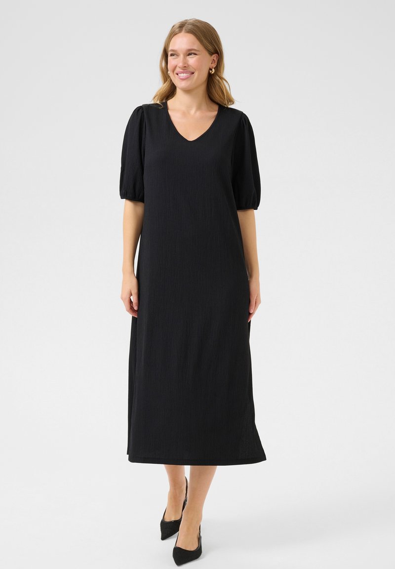 Black puff-sleeve dress with a V-neck, knee-length, textured fabric, and a straight silhouette. Worn with pointed black heels.