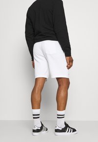 Vita shorts med bakficka, parat med en svart långärmad tröja, svarta sneakers och randiga vita strumpor. Slät tygtextur.