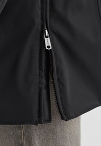 Schwarze Jacke mit einer glatten, matten Textur und silbernem Reißverschluss-Detail. Hat ein eng anliegendes Design ohne sichtbare Muster.