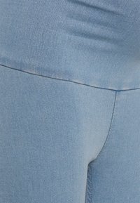 Tecido de denim azul claro, design ajustado com textura suave, costura visível ao longo das costuras, sem padrões ou ferragens distintas.
