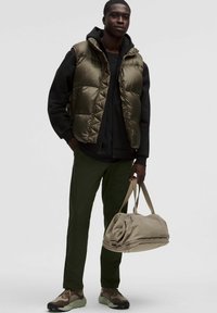 Sooja oliivivärvi vest musta kapuutsiga särgi peal, rohelised püksid ja pruunid tened. Kätel on beež duffel kott, millel on külgpikk tõmblukk ja ribasingid.