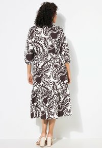 Kukallinen mekko, jossa on viskoosikangas, pehmeä rakenne, kolmivartiset hihat, kerrostettu helma ja ruskea-valkoinen väriyhdistelmä.