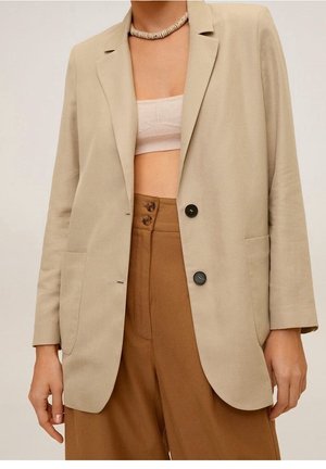 Beige blazer med to sorte knapper over en beige cropped top, kombineret med højttaljede brune bukser med vide ben og en perlekæde.