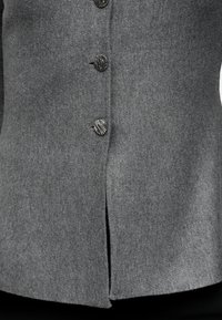 Gros plan d'un cardigan gris en maille côtelée avec quatre boutons ronds texturés noirs et blancs fermés au centre devant.