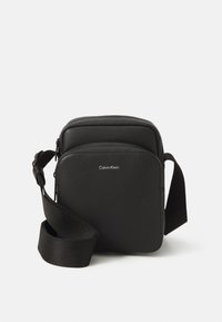 Borsa a tracolla nera in similpelle testurizzata, di forma rettangolare, con tracolla regolabile e dettaglio del logo frontale.