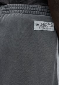 Γκρι αθλητικό σορτς από μαλακό ύφασμα, με ελαστική μέση, πλαϊνές ρίγες και ανοιχτό γκρι ετικέτα με το λογότυπο "Adidas Originals".