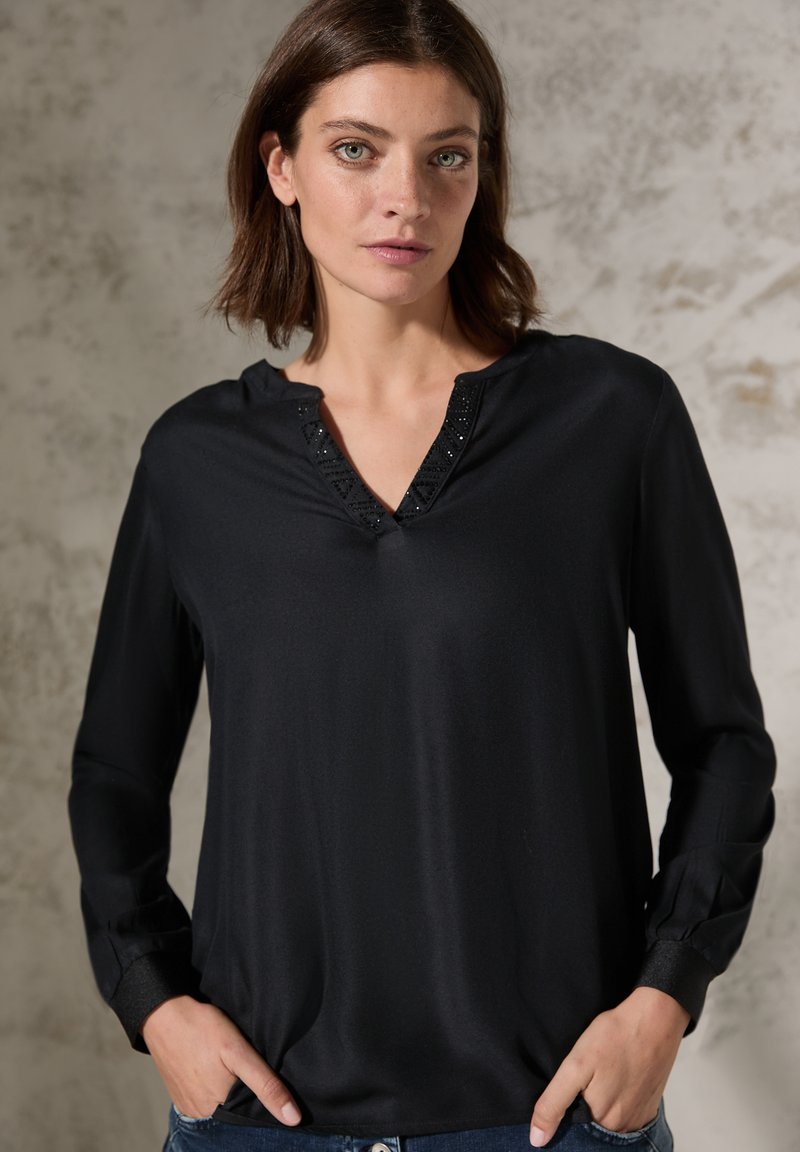 Blusa nera a maniche lunghe con scollatura a V decorata con accenti decorativi. Tessuto morbido e vestibilità rilassata, arricchita da polsini con bottoni.