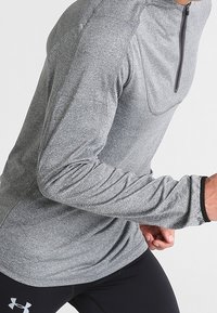 Camiseta deportiva de manga larga en color gris con cuello alto y cierre de cremallera de cuarto, hecha de tela texturizada que absorbe la humedad, diseño ajustado.