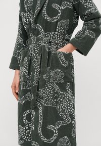 Rochie de culoare verde închis cu un finisaj texturat, având un model cu imprimeu de leopard alb. Vine cu o curea și buzunare frontale.