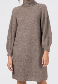 Turtleneck klänning i ljusbrunt, tillverkad av mjukt strukturerat material. Har ballongärmar och fåll som slutar ovanför knäna.