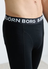 Boxers masculinos pretos com uma ampla cintura preta que apresenta o texto “BJÖRN BORG” em cinza. O tecido é suave e com um ajuste justo.