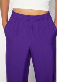Fialové kalhoty s elastickým páskem a bočními kapsami, s hladkou texturou a volným střihem. Vhodné pro každodenní nošení nebo sportovní aktivity.