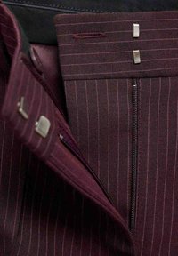 Temno burgundska tkanina z tankimi navpičnimi črtami, ki vsebuje zadrgo in kovinske sponke. Material se zdi teksturiran in gladek.