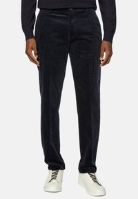 Dark blue corduroy trousers with visible vertical ridges, button closure, and side pockets. Paired with white slip-on sneakers.