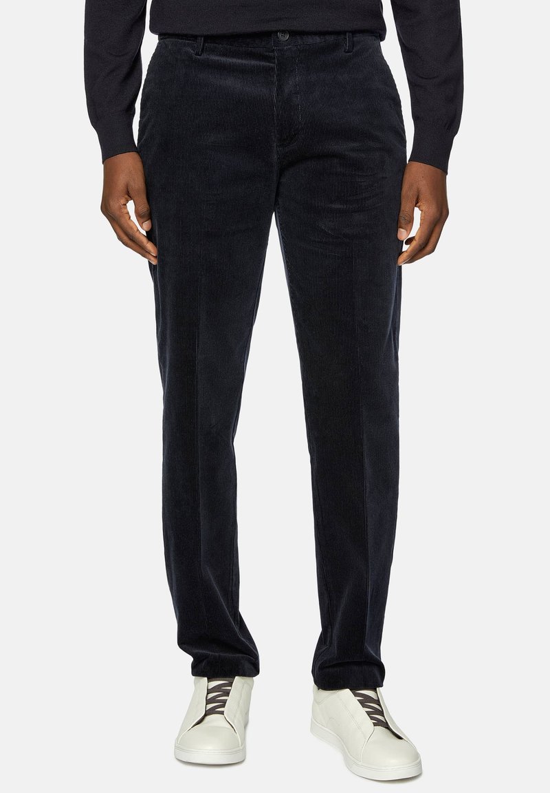 Dark blue corduroy trousers with visible vertical ridges, button closure, and side pockets. Paired with white slip-on sneakers.