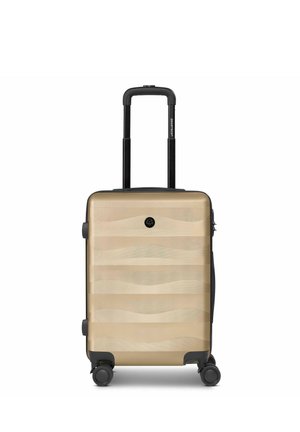 Valigia compatta beige con guscio rigido, design a onde texturizzate, quattro ruote nere girevoli e manico telescopico nero estensibile.