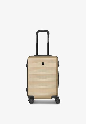 Valigia compatta beige con guscio rigido, design a onde texturizzate, quattro ruote nere girevoli e manico telescopico nero estensibile.