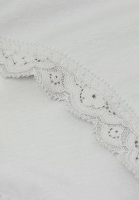 Lichtgrijze stof met een delicate kantafwerking met bloemprint en geschulpte randen aan één kant. Zachte textuur en een gladde afwerking.
