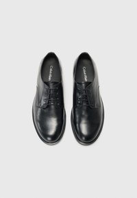 Zwarte leren veterschoenen met een gladde textuur, ronde neus en subtiele branding op de inlegzolen. Voorzien van zes oogjes en een minimalistisch ontwerp.