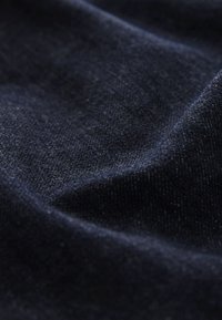 Detail tmavomodrej denimovej látky zobrazujúci jej textúrované tkanie a jemné záhyby.